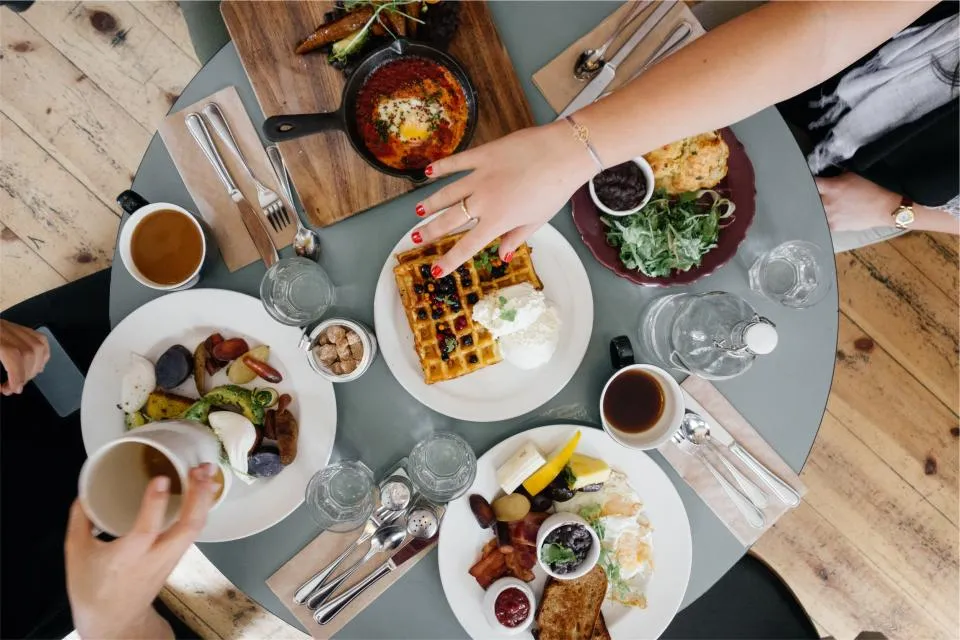 A table spread with waffles, shakshuka, salads and coffee, seen from above