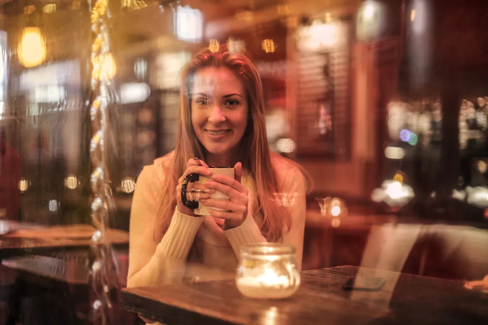 A woman smiling over a mug of coffee in a warmly lit cafe